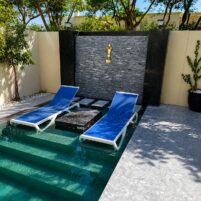 Luxury swimming pool Dubai with submerged lounge chairs, decorative wall, and landscaping